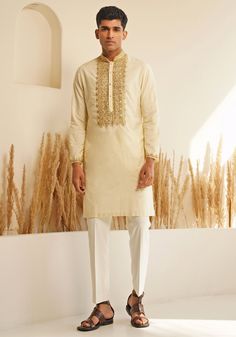 Presenting the Ivory And Gold Silk Kurta Set with a chinese collar for elegance and metallic golden buttons for a unique detail. The hand embroidered details on the neckline and cuffs make it stand out. Teamed with elegant white pants. Perfect for an Engagement, Roka or Wedding Reception. Composition : Chanderi Silk Care: Dry Clean Only and Vacuum Storage This product can be customized for sleeves, length and colour Delivery : 4-6 weeks as the product is hand crafted. Check Size Guide or choose MySize for free customisation (All Sizes above XL can be made at 15% additional cost) For more information and sizes please contact fabiliciousfashion@gmail.com or visit our Copenhagen studio. About the Designer : Shreyansh, a distinguished designer label specializing in luxurious ethnic menswear fo Traditional Sets With Embroidered Neckline For Festivities, Traditional Wedding Sets With Embroidered Neckline, Festive Designer Traditional Wear With Embroidered Neckline, Traditional Festive Sets With Embroidered Neckline, Designer Kurta With Resham Embroidery And Stand Collar, Designer Resham Embroidery Kurta With Stand Collar, Eid Fitted Kurta With Embroidered Cuffs, Designer Embroidered Cuff Kurta For Eid, Stand Collar Kurta With Resham Embroidery