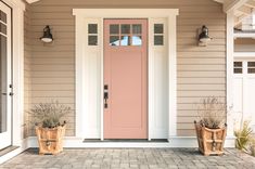 two planters on the front porch of a house with pink door and white trim