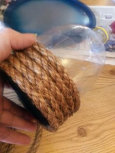 a person is holding a bottle with rope wrapped around it on a wooden table top