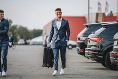 two men in suits are walking down the street with their suitcases and one is carrying a suit case