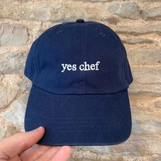 "Introducing our stylish cap featuring the words \"Yes Chef\" embroidered on the front in a minimalist font. Made with high-quality materials, this cap is perfect for those who want to make a statement while keeping it simple. Not only does this cap feature a bold statement, but it also offers the option for customisation. You can add your initials or name on the back of the cap to make it truly unique to you. Cap Styles/Colourways: We have two cap styles that you can choose from: CLASSIC: The classic cotton dad cap has an unstructured, low profile styling, and features an adjustable buckle on the back, ensuring a comfortable and secure fit for all head sizes. Choose from any of our classic colours: Navy, Black, Beige, Pale Blue, Pink, Mint Green, Lemon. CORDUROY: The corduroy cap is made Xmas Gift Ideas For Friends, Chef Cap, Yes Chef, Art Merch, Corduroy Cap, Minimalist Font, Cool Gift Ideas, Stylish Caps, Hijabi Aesthetic