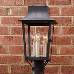 three candles are lit in an old fashioned lantern on a street light pole against a brick wall