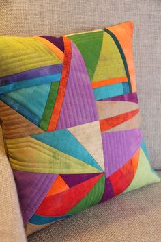 a colorful pillow sitting on top of a couch next to a beige chair and arm rest