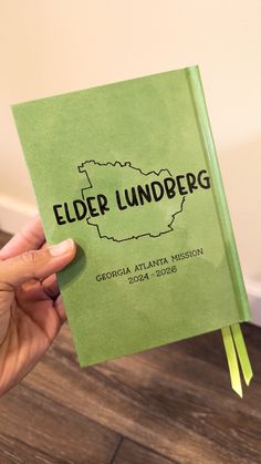 a person holding up a green book with the word elder lindenberg written on it