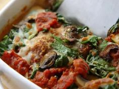 a casserole dish with spinach, mushrooms and tomatoes in it on a table