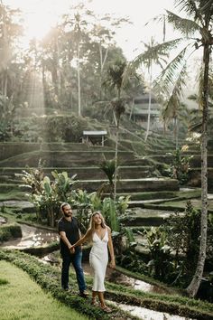 a man and woman holding hands while walking through the grass in front of some palm trees