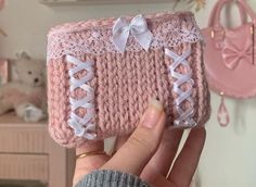 a hand holding up a pink crocheted purse with white laces and bows