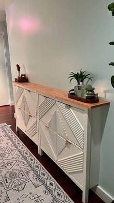 a white dresser with plants on top and a rug in the corner next to it