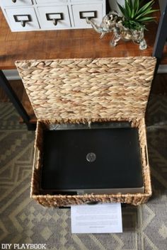 an open laptop computer sitting on top of a wicker box next to a plant