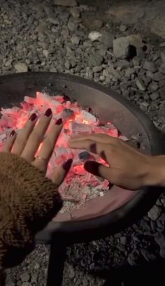 two hands reaching for something in a pan on the ground with rocks and gravel around it