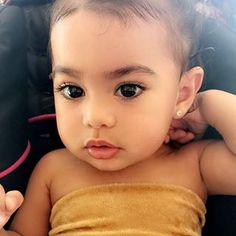 a baby in a car seat with her hand on her head and looking at the camera