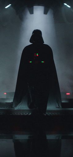 the silhouette of darth vader stands in front of fog and lights on stage