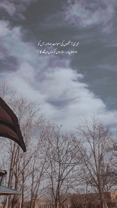 an open umbrella sitting on top of a wooden bench under a cloudy sky with trees in the background