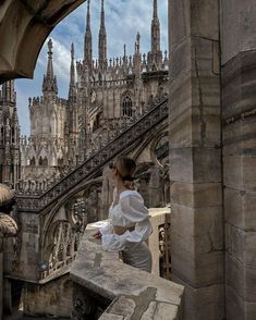 a woman standing on top of a stone building next to a stair case in front of a cathedral