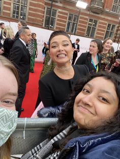 two women smile as they stand on the red carpet in front of a group of people