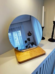 a round mirror sitting on top of a counter next to a lamp and candle holder