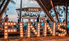 the word finns is lit up in front of people sitting on lounge chairs under palm trees