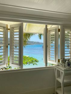 an open window with white shutters overlooking the ocean