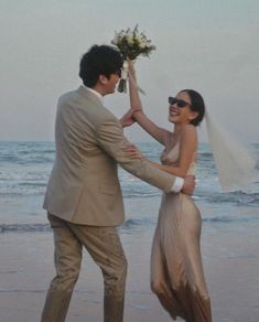 a man and woman standing on top of a beach next to the ocean holding each other's hands