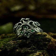 a silver ring with green stones sitting on top of a rock