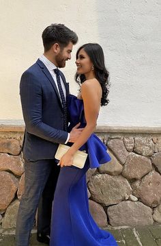 a man and woman in formal wear standing next to each other on a stone wall