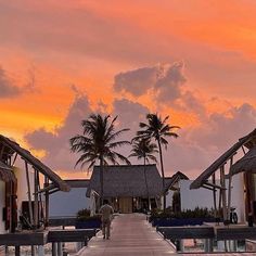 a walkway leading to the beach with thatched huts and palm trees in the background