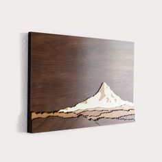 a wooden wall hanging with a mountain scene painted on it's side in brown and white