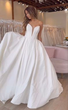 a woman in a white wedding dress is standing near a couch and looking at the camera