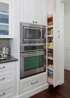 a stainless steel oven and microwave in a white kitchen with wood flooring, built - in shelving