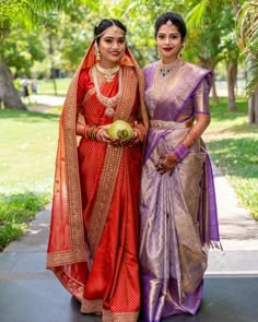 two women standing next to each other on a sidewalk with trees in the back ground