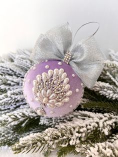 a purple ornament with silver bow on top of snow covered pine tree branches