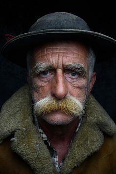 an old man with a mustache and a hat on his head is looking at the camera