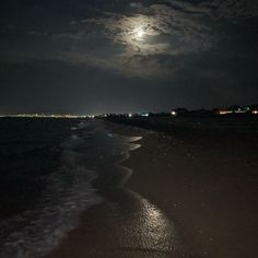 the full moon is shining over the water at night on the beach with waves coming in