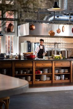 a man standing in a kitchen preparing food with pots and pans hanging from the ceiling