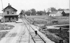 an old black and white photo of a man walking on train tracks in front of a house