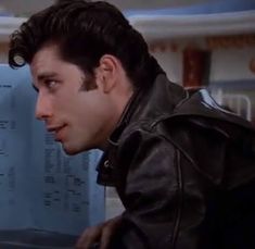 a man in a leather jacket looking at a computer screen with information on the wall behind him