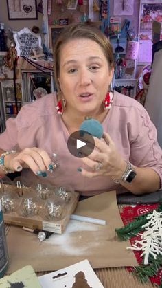 a woman is sitting at a table making ornaments