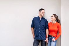 a man and woman standing next to each other in front of a white wall smiling