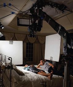 a man laying on top of a bed in a room filled with lights and equipment