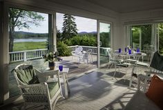 a porch with chairs, tables and windows overlooking the water is shown in this image