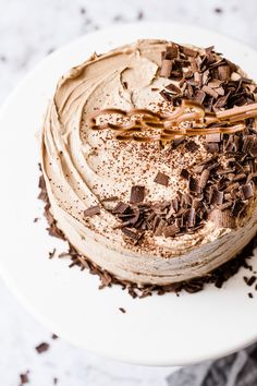 a white plate topped with a cake covered in frosting and chocolate shavings