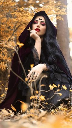 a woman with long black hair sitting in the woods