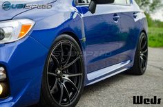 the front end of a blue subarunt car with black rims and chrome wheels