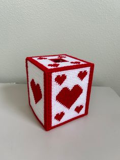 a red and white cross stitched cube with hearts on the side sitting on a table