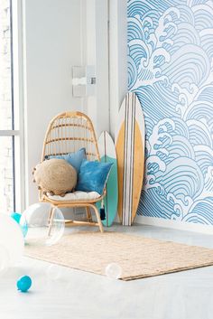 a surfboard is next to a chair and rug in front of a wall with blue waves on it