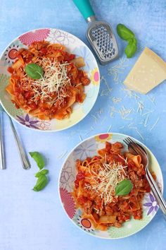 two bowls filled with pasta and sauce on top of a blue table