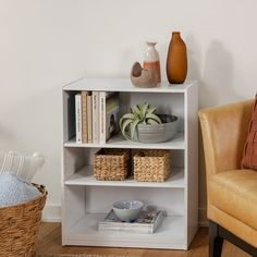 a white book shelf with baskets and vases on it next to a brown chair