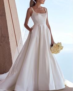 a woman in a white wedding dress holding a bouquet and looking off into the distance