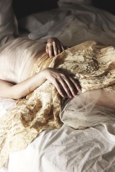 a woman laying on top of a bed covered in white sheets and blankets with her hands resting on the pillow