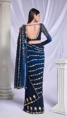 Our midnight blue pre-stitched sari, expertly crafted from a blend of georgette and tulle fabrics, features a delicate floral border adorning the tulle bottom, while the georgette pallu is elegantly embroidered with lines of pearls, metallic details, and acrylics. Paired with this sari is a georgette full-sleeve blouse, featuring metallic motifs and embellished with lines of pearls, golden bricks, and intricate motifs. Blue Pre-draped Saree With Mirror Work, Traditional Blue Blouse Piece For Evening, Blue Georgette Pre-draped Saree For Evening, Blue Traditional Drape Blouse For Evening, Evening Georgette Pre-draped Saree With Mirror Work, Evening Pre-draped Saree In Georgette With Cutdana, Traditional Drape Blue Blouse Piece For Evening, Elegant Blue Pre-draped Saree For Festive Occasions, Evening Pre-draped Cutdana Georgette Saree